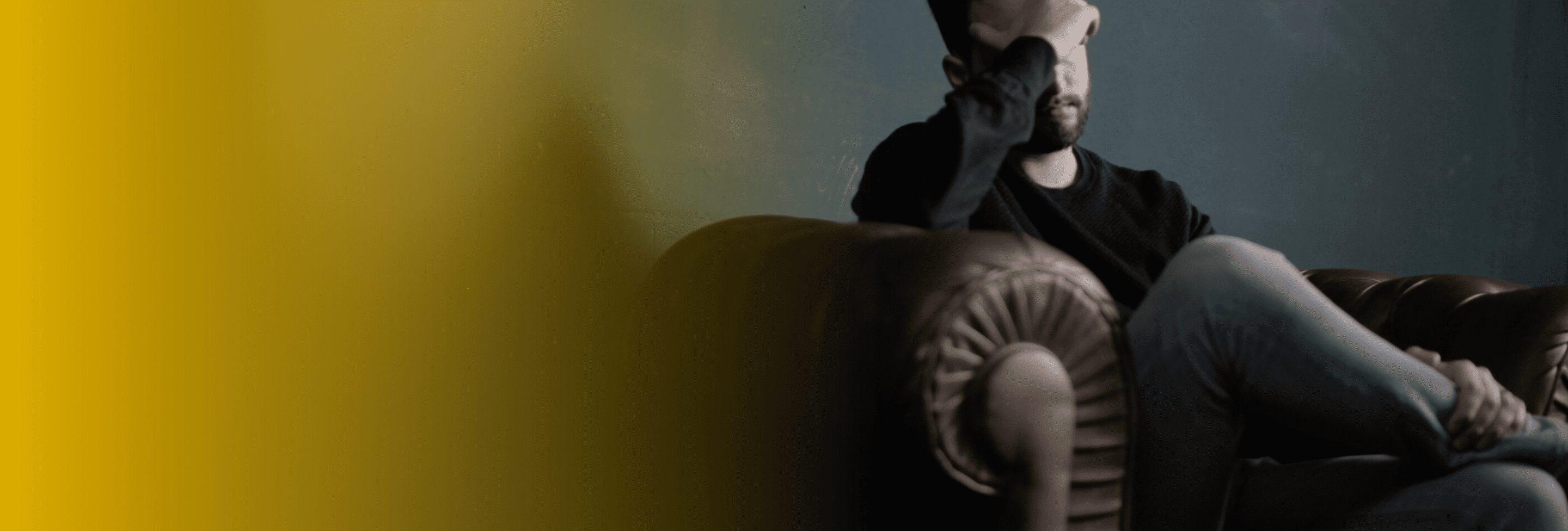 Man sitting on couch with hand covering face in dark room